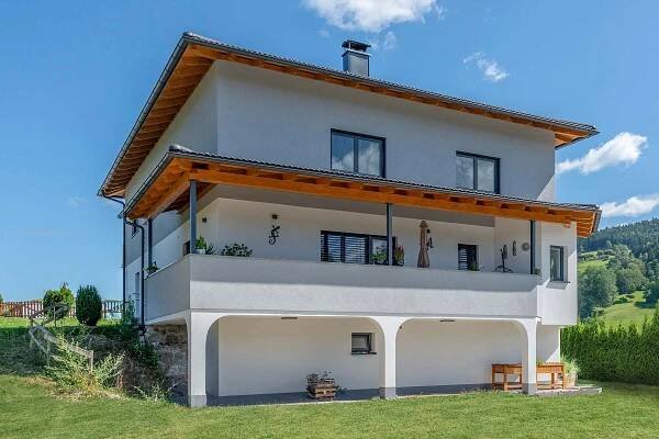 Modernisiertes Einfamilienhaus in Österreich mit Holzveranda und weißer Fassade, ideal für mehr Wohnraum durch Aufstockung.