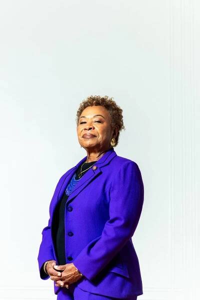 Barbara Lee standing for a portrait wearing a purple suit jacket and a black shirt.