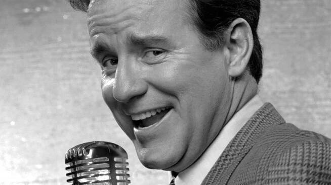 phil hartman in suit smiling with microphone