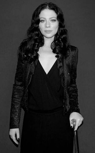A black-and-white photo of Michelle Trachtenberg, a thin woman with long dark hair dressed elegantly in black and looking expressionlessly at the camera.