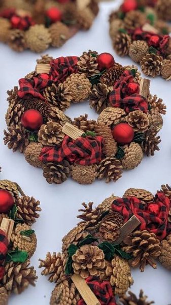 pine cone wreaths with red and black plaid bows are arranged on a white table