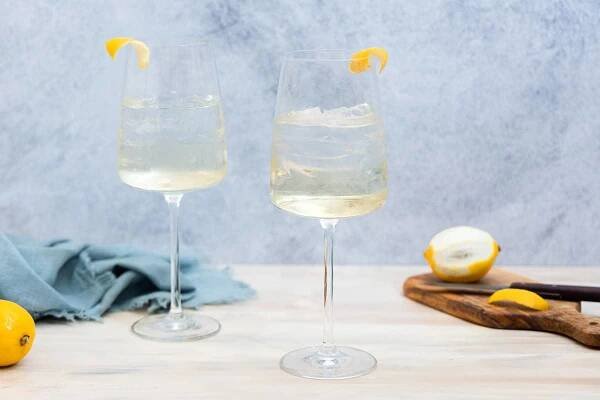 Two wine glasses filled with ice and an almost clear liquid, both with lemon twist garnishes.