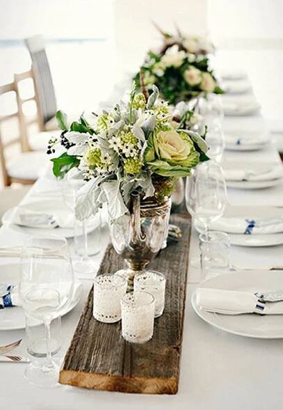 the table is set with white and green flowers in glass vases on wooden planks