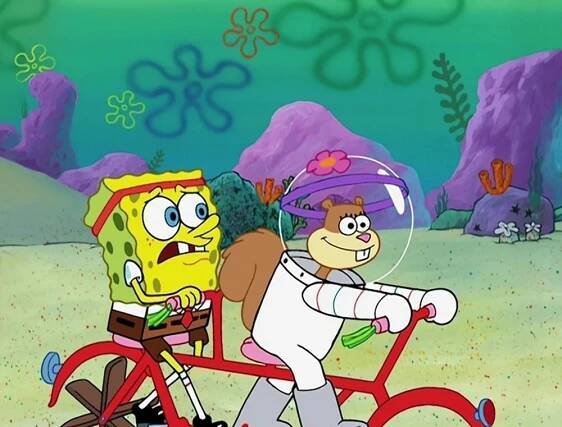 SpongeBob SquarePants and Sandy Cheeks riding a tandem bicycle underwater. SpongeBob looks worried while Sandy smiles confidently