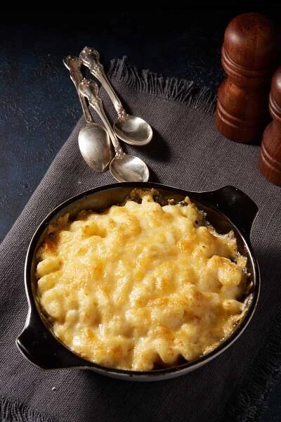 Baked macaroni and cheese in a round baking dish on a napkin with spoons. 