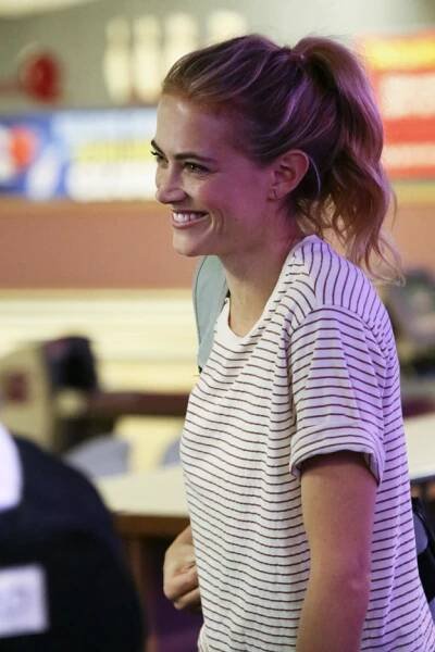 a woman with purple hair smiles at the camera while standing in front of other people
