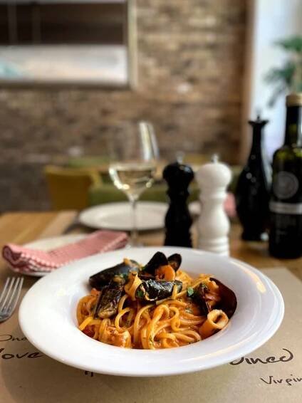 a plate of pasta with mussels and wine on the side at a restaurant