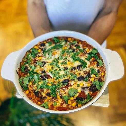 a person holding up a pizza in a white casserole dish on top of a wooden table