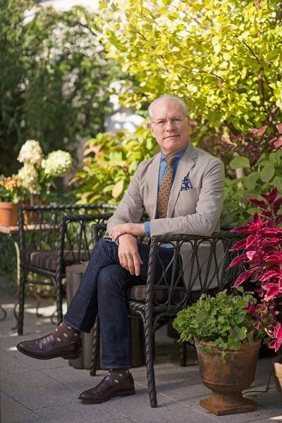 A person seated on an outdoor terrace with green plants in the background
