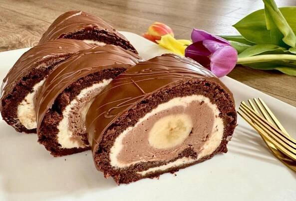 there is a chocolate roll on the plate next to a fork and flower with flowers in the background