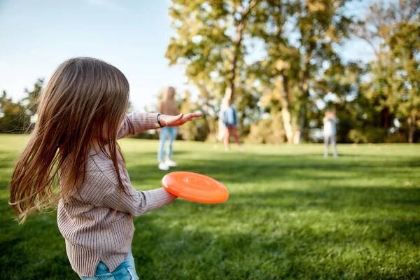 Vytváření vzpomínek, prolomení vzdálenosti. Malá dívka hraje frisbee se svou rodinou v parku za slunečného dne stock fotka