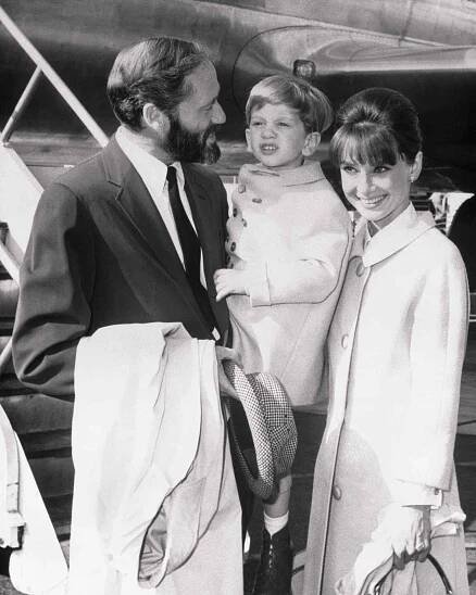 A mother and father with their toddler son standing in front of an airplane in 1963.