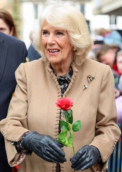 Queen Camilla smiles after receiving a red rose from Abi Crighton during her visit to the Farmers' Market on March 27, 2024
