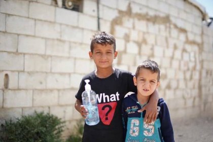 2 Syrian boys hold hand sanitiser, one with the arm around the other, outside in Lebanon 