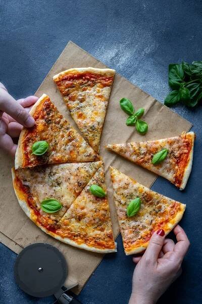 Overhead shot of Quick and Easy Pizza, sliced. Two hands are grabbing slices of the pizza.