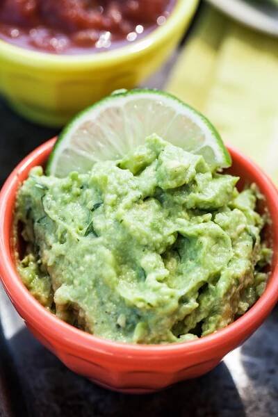 fresh, single serve quacamole garnised with a slice of lime served in a small orange bowl