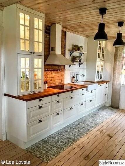 an empty kitchen with white cabinets and wood flooring is pictured in this image, there are two pendant lights hanging from the ceiling