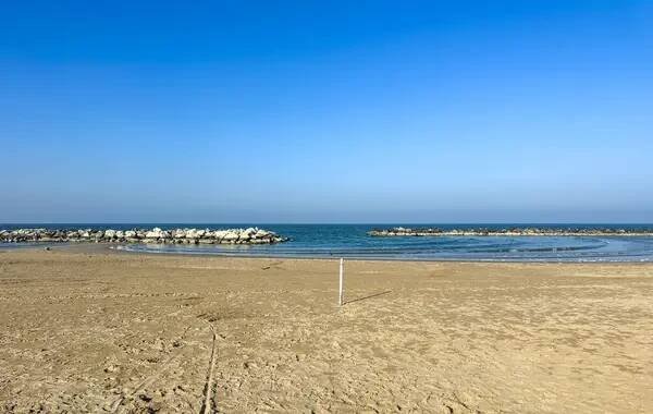 Široká, prázdná pláž v Misano Adriatico, Rimini v zimě. Jasná obloha nad písčitým pobřežím se vzdálenými budovami a klidným mořem. Kvalitní fotografie — Stock obrázek