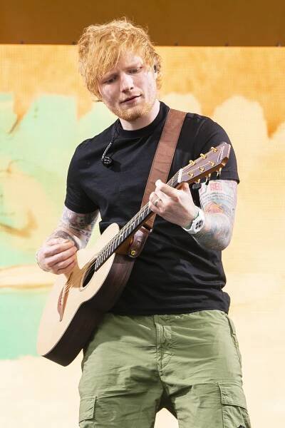 Ed Sheeran performing at a music festival, playing an acoustic guitar.