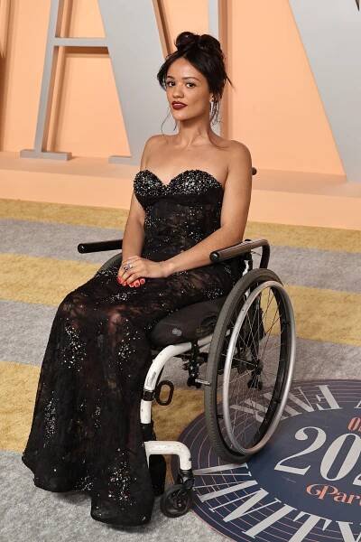 Marissa Bode in a wheelchair wearing a strapless, sequined black gown on a red carpet. Hair styled up, with elegant and confident demeanor