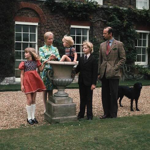 A family group of a woman man and three children in light casualformal attire standing outside in a garden and conversing