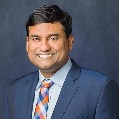 John Samuel, Founder of ABLR smiling at the camera wearing a blue suit and a blue and orange plaid tie