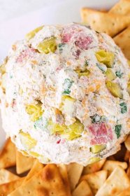 Top down close up view of a dill pickle cheese ball surrounded by pita chips, showing off the dill pickles and salami within the cream cheese.