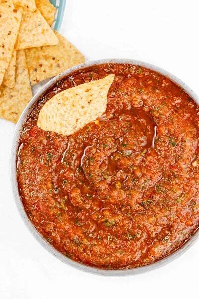 A bowl filled with chunky salsa topped with a single tortilla chip, with a few tortilla chips placed beside the bowl.