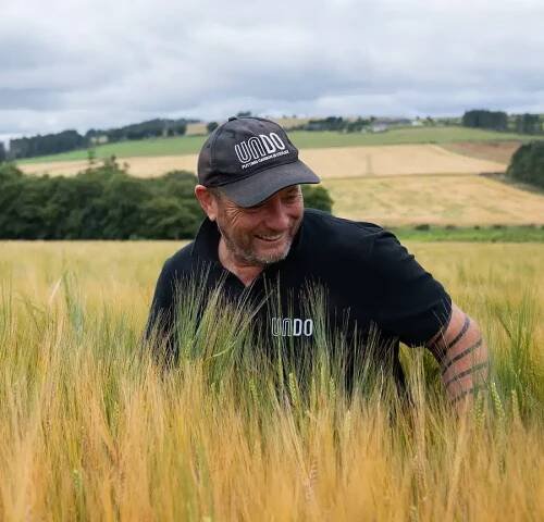 Man in a black shirt and hat standing in a UK barley field