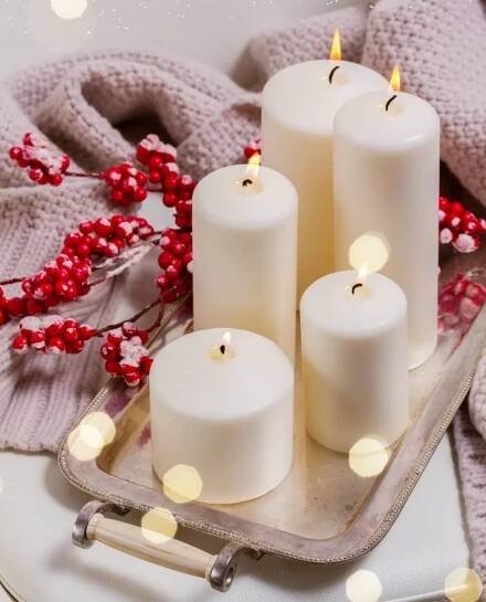 5 lit candles on a tray decorated with a spray of frosted cranberries and a woolly throw.