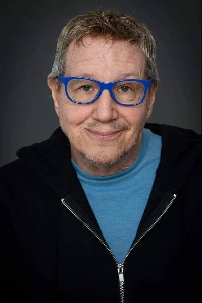 Headshot of Paul Gordon. Paul is wearing a navy blue jacket over a teal shirt. He is also wearing Royal Blue glasses