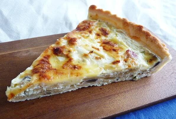 a piece of quiche sitting on top of a wooden cutting board
