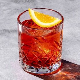Vibrant red Mezcal Negroni in etched rocks glass on marble background, with orange garnish
