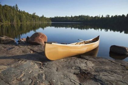 Žluté kanoe na skalnatém břehu jezera klidu s borovicemi — Stock obrázek
