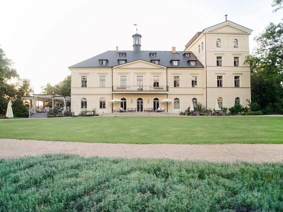 The elegant Chateau Mcely, featuring a vast mansion and a vibrant green lawn.