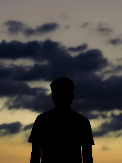 A silhouette stands before a cloudy sunset.