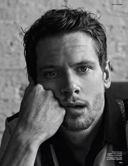 a black and white photo of a man with his hand on his face looking at the camera