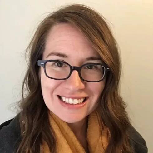 Woman with glasses and brown hair smiling warmly against neutral background