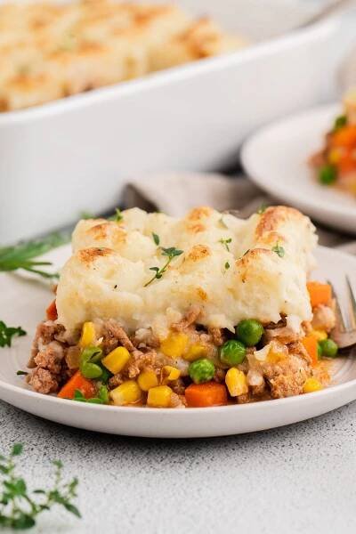 A white plate of ground turkey shepherd's pie with a baking dish in the background