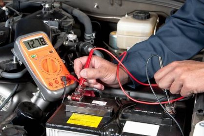 Stáhnout - Automechanik používá multimetr voltmetr kontrolovat hladinu napětí v autobaterii. — Stock obrázek