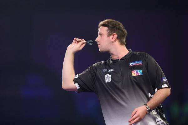 a man wearing a shirt that says gks throws a dart