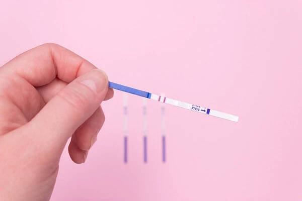 ruka drží pozitivní těhotenský test na růžovém pozadí - ovulace - stock snímky, obrázky a fotky