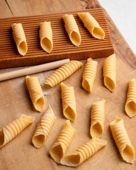 Homemade garganelli pasta on a wooden cutting board. Gnocchi board and wooden dowel with finished pasta shapes sitting on top.