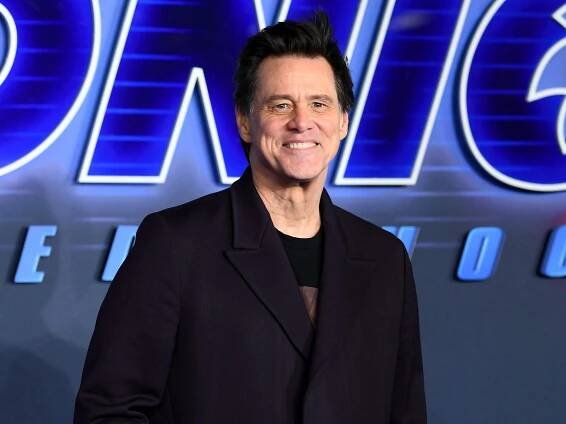 Jim Carrey wearing a black jacket in front of a Sonic the Hedgehog sign.