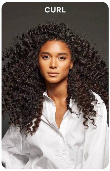 Model with long, voluminous, defined curls wearing a white button-up shirt against a dark gray background. Bold white text above reads: “CURL.”