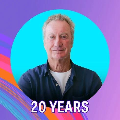 Actor Bryan Brown smiles. He is standing in front of a purple background, the text below him says "20 years".