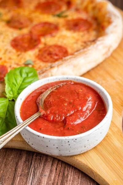 a spoon in a small bowl of smooth tomato pizza sauce.