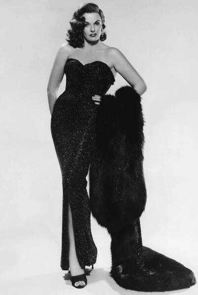 an old photo of a woman in a black dress posing with a fur coat on