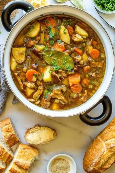 Top down view of a pot with vegetables in a brown liquid with a sliced baguette below it