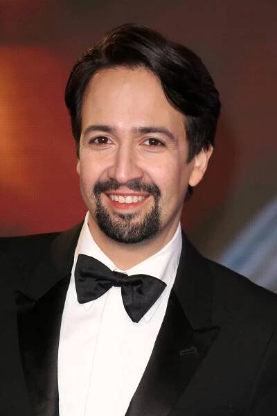 Lin-Manuel Miranda smiles while posing for a picture in a suit.
